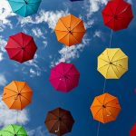 A photograph of brightly coloured umbrellas, strung in the sky.