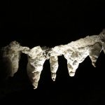A photograph of stalactites lit dramatically against a black background.