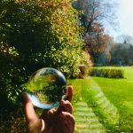 A photograph of a hand holding a glass sphere that reflects the surrounding landscape.