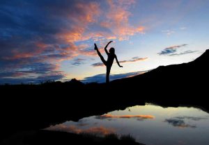 A photograph of a dancer silhouetted against a sunset reflected in a pond.