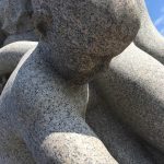 Photograph of human-shaped rock sculpture looking down.