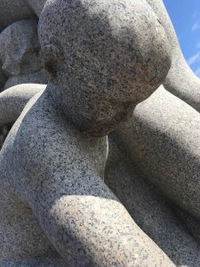 Photograph of human-shaped rock sculpture looking down.
