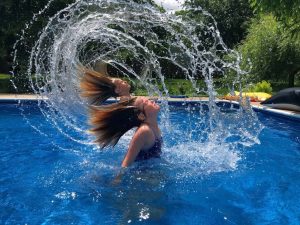 A photograph of twin girls in a pool flicking their water-soaked hair in an arc.