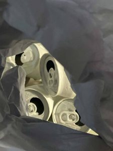 A mixed media image of aluminum cans painted white, seen through crinkled grey paper.