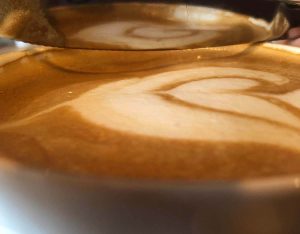 A close-up photograph of a hot drink reflected in a butter knife.